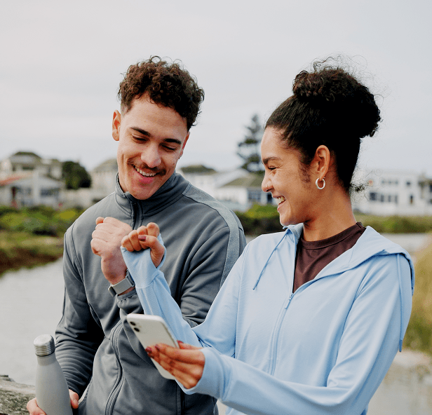 Two people outdoors smiling and looking at a smartphone