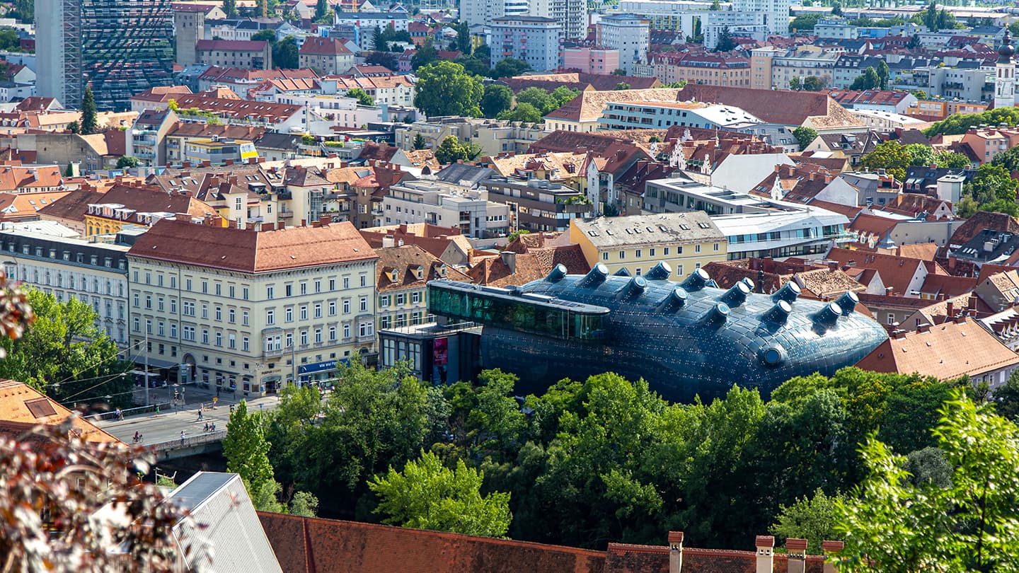 European City Aerial View with Historic Architecture Aerial view of a European city with historic buildings, red-tiled roofs, and a distinctive modern dark building with curved architecture among traditional architecture.
