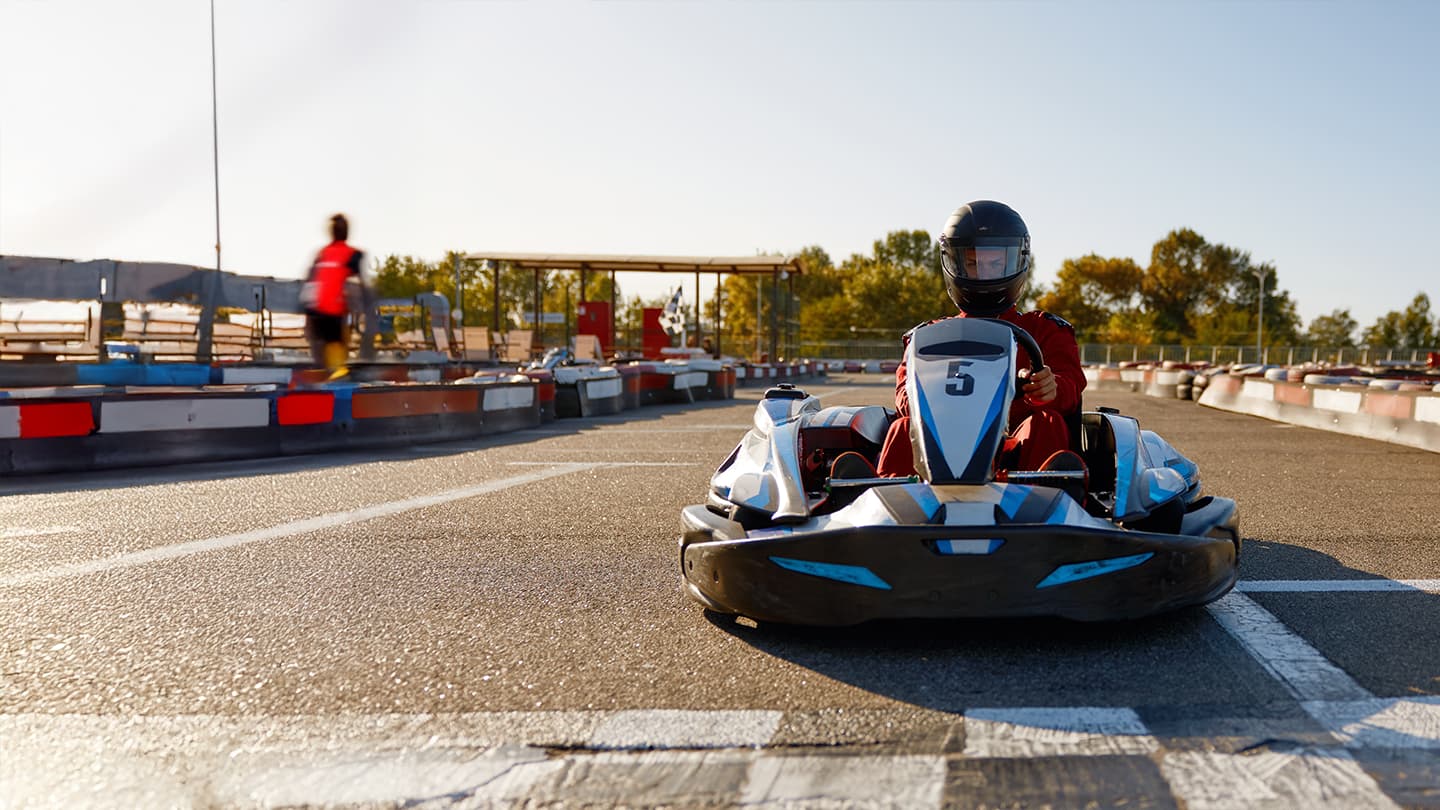 Go-Kart Racing on Outdoor Track Go-kart driver in helmet and red suit on outdoor racing track