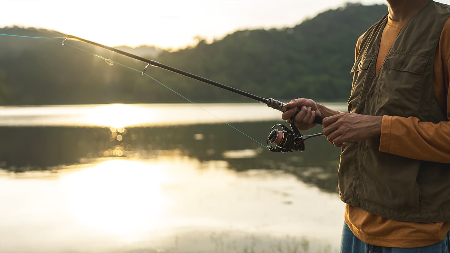 Lakeside Fishing at Golden Hour Man casting a spinning rod on a calm lake at sunset