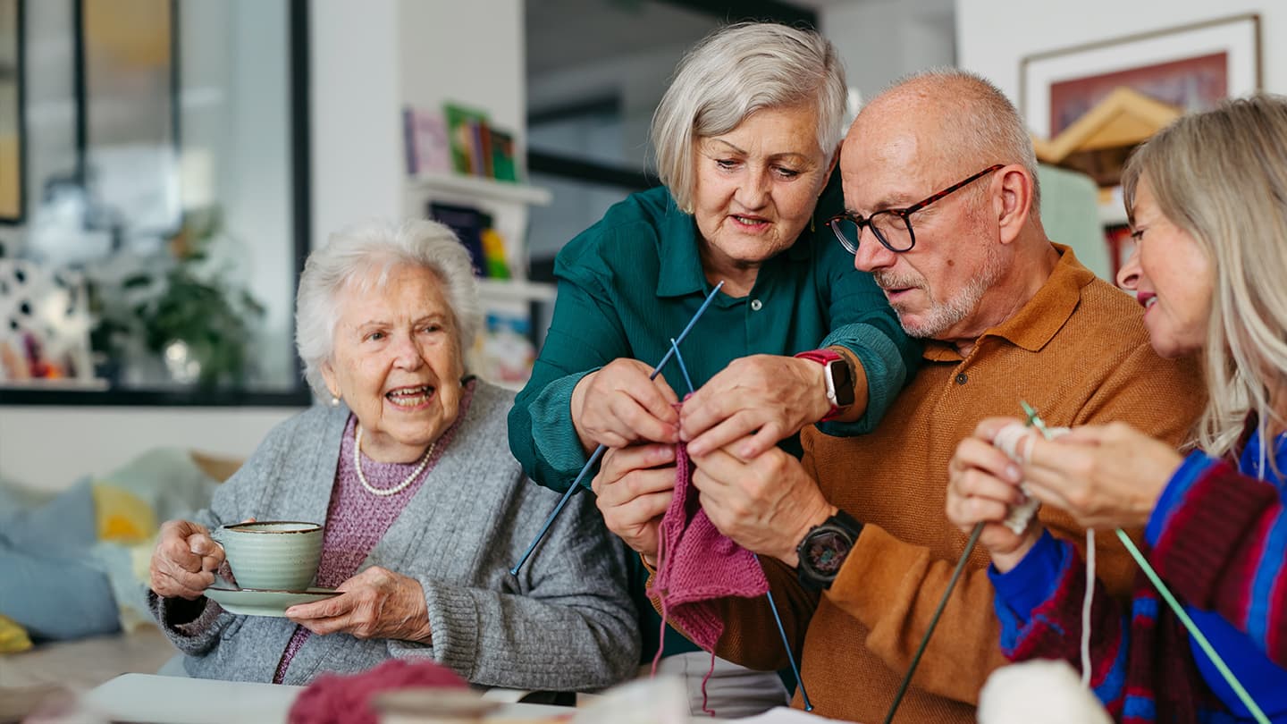 Seniors Enjoying a Group Knitting Activity Group of seniors knitting together and laughing in a cozy living room
