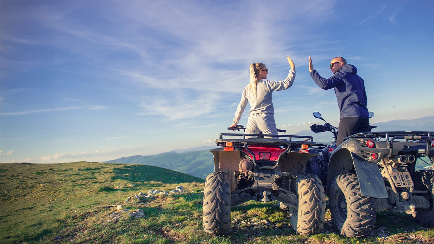 Couple Celebrating on Mountain ATVs Two ATV riders high-fiving on a scenic mountain ridge