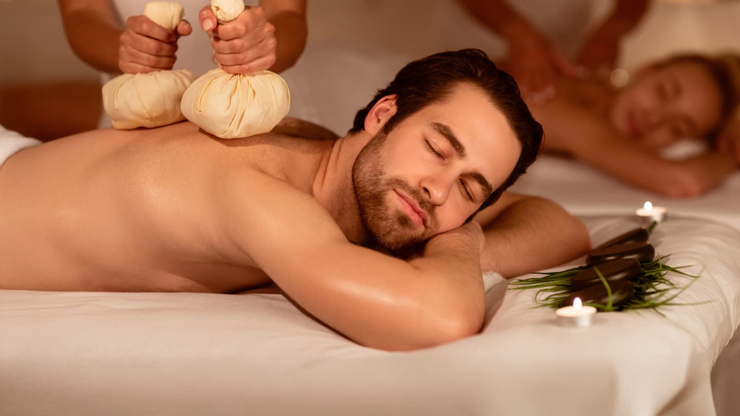 Couples Herbal Compress Spa Massage Man receiving Thai herbal compress massage at luxury spa with woman in background