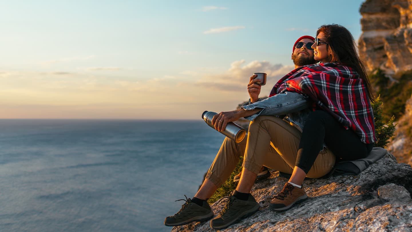 Couple Resting on Coastal Cliff at Sunset Couple sitting on a coastal cliff at sunset with hiking gear