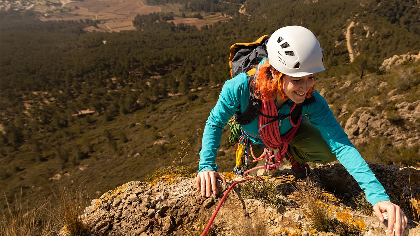 Woman Rock Climbing Mountain Summit Smiling woman in helmet climbing rocky mountain ridge with rope and gear