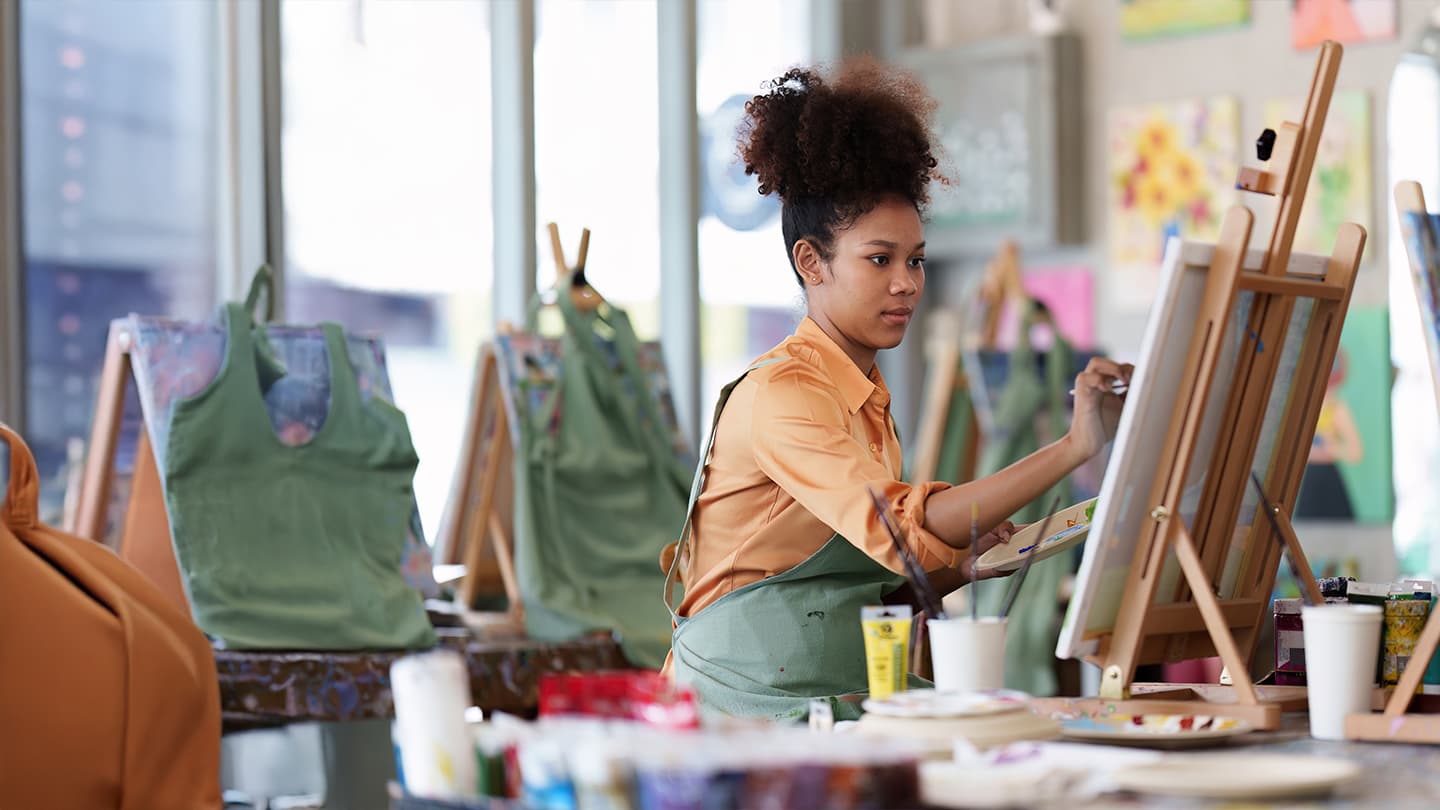 Woman Painting in Art Studio Class Young woman painting on canvas at an easel in an art studio