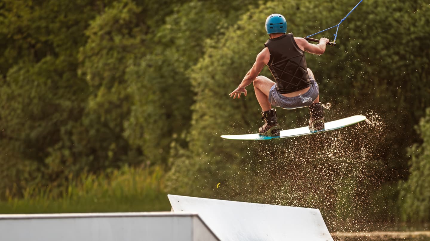 Wakeboarder Jumping Ramp at Cable Park Wakeboarder in blue helmet performing aerial jump off ramp at cable wake park with water spray