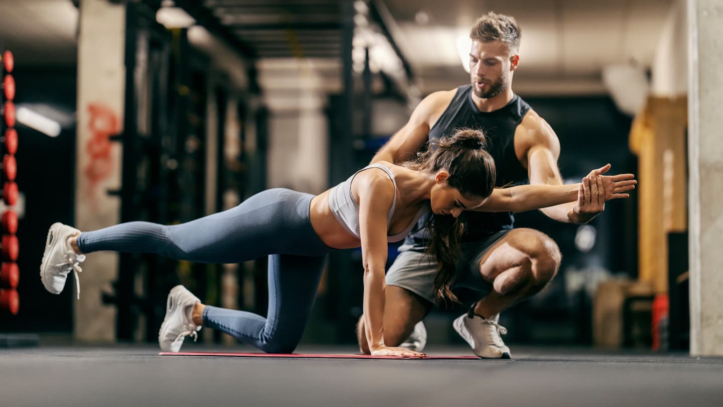 Personal Trainer Coaching Core Workout Male personal trainer guiding woman through core stability exercise on gym floor