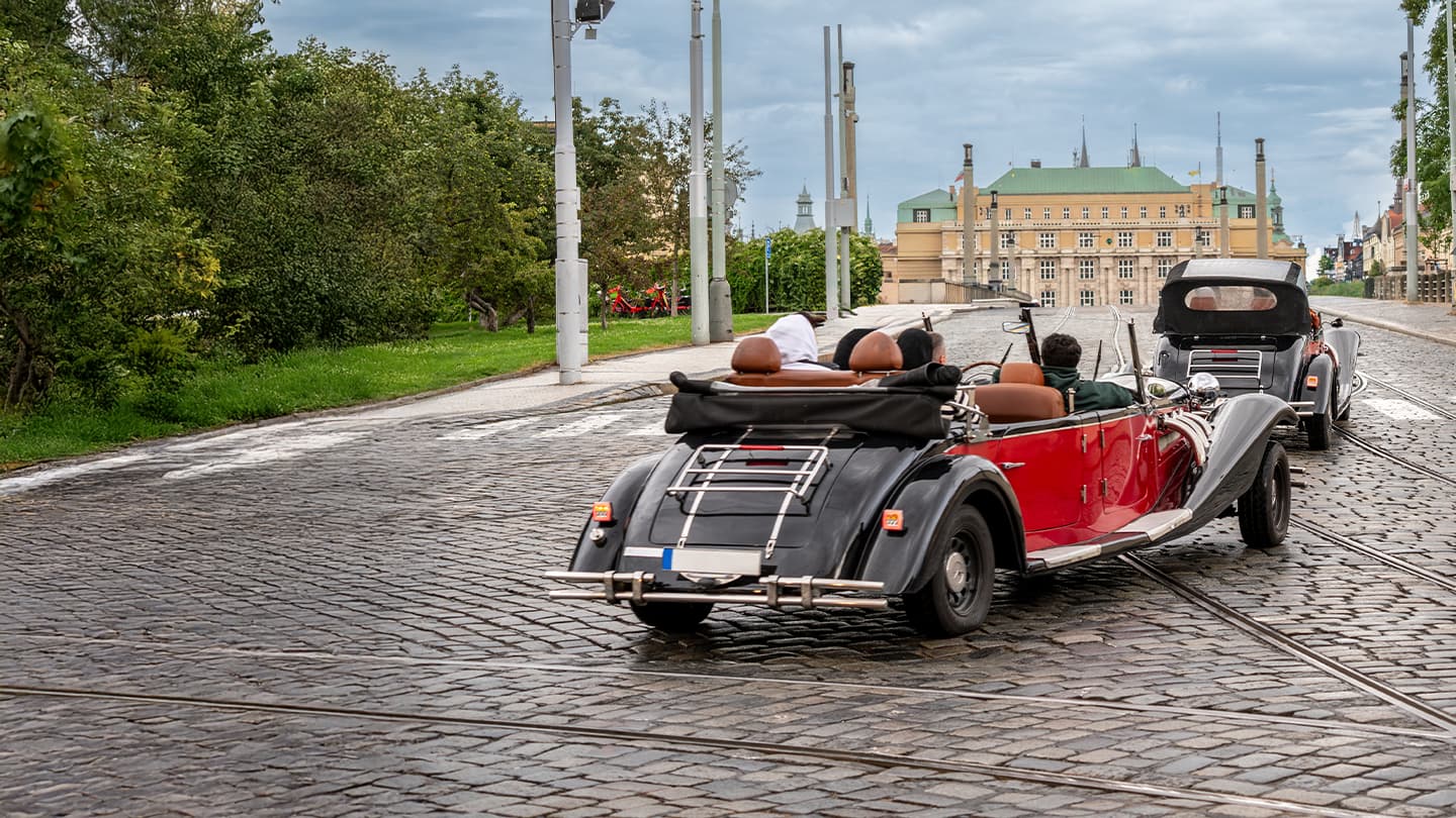 Vintage Car Tour on Cobblestone Streets Two vintage convertible cars driving on a cobblestone street toward a historic building