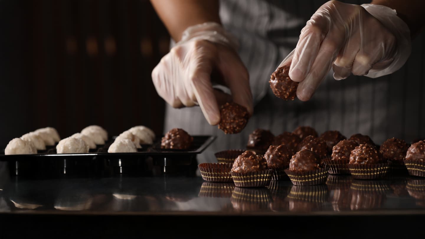 Artisan Chocolate Truffle Making Gloved hands placing handcrafted chocolate truffles into paper cups