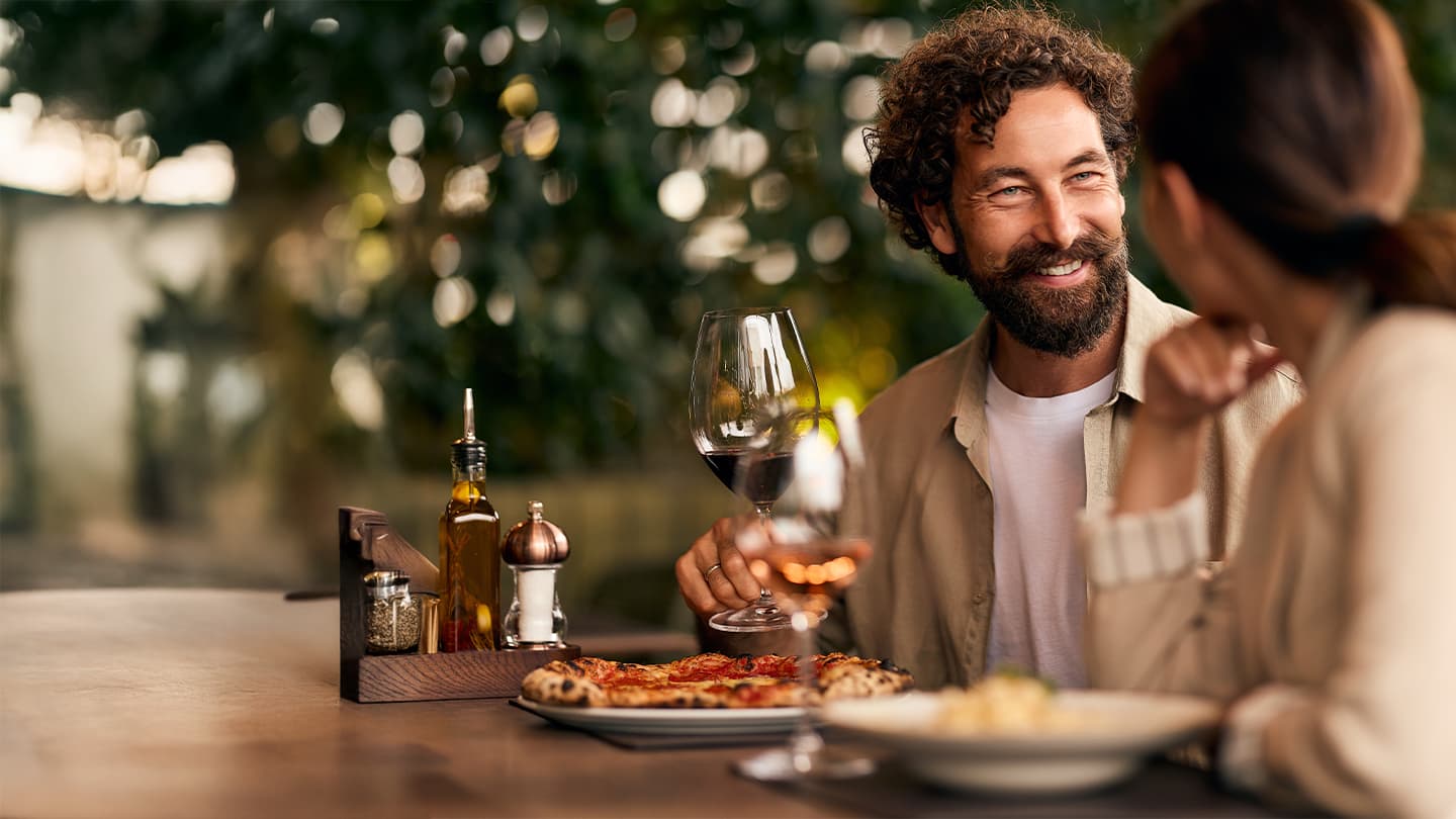 Outdoor Dining with Wine and Pizza Smiling man holding red wine at outdoor restaurant table with pizza