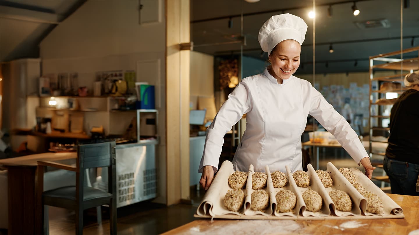 Baker Preparing Fresh Seeded Bread Rolls Smiling baker placing seeded bread rolls on a proofing cloth in a bakery