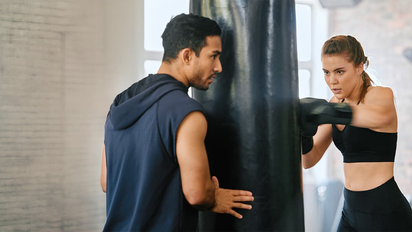 Boxing Training With Heavy Bag Two people practicing boxing drills with a heavy bag in a bright gym setting.