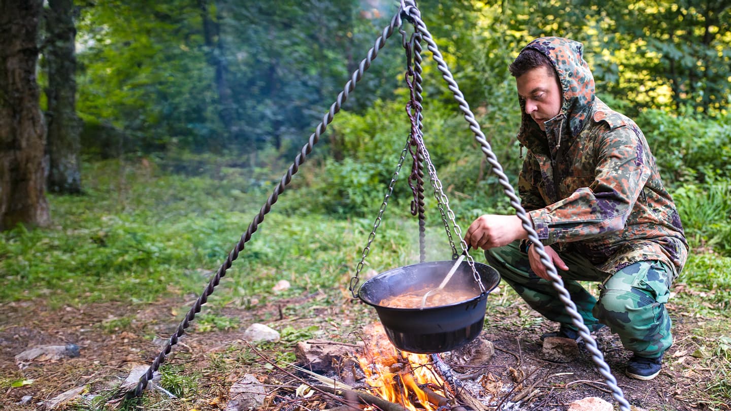 Outdoor Campfire Cooking in the Forest Man in camouflage gear stirring a pot over a campfire in the forest