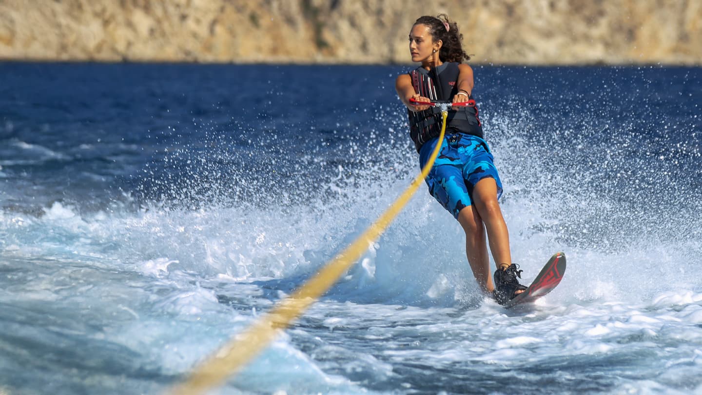 Woman Water Skiing Near Rocky Coast Young woman water skiing on blue ocean near rocky cliffs