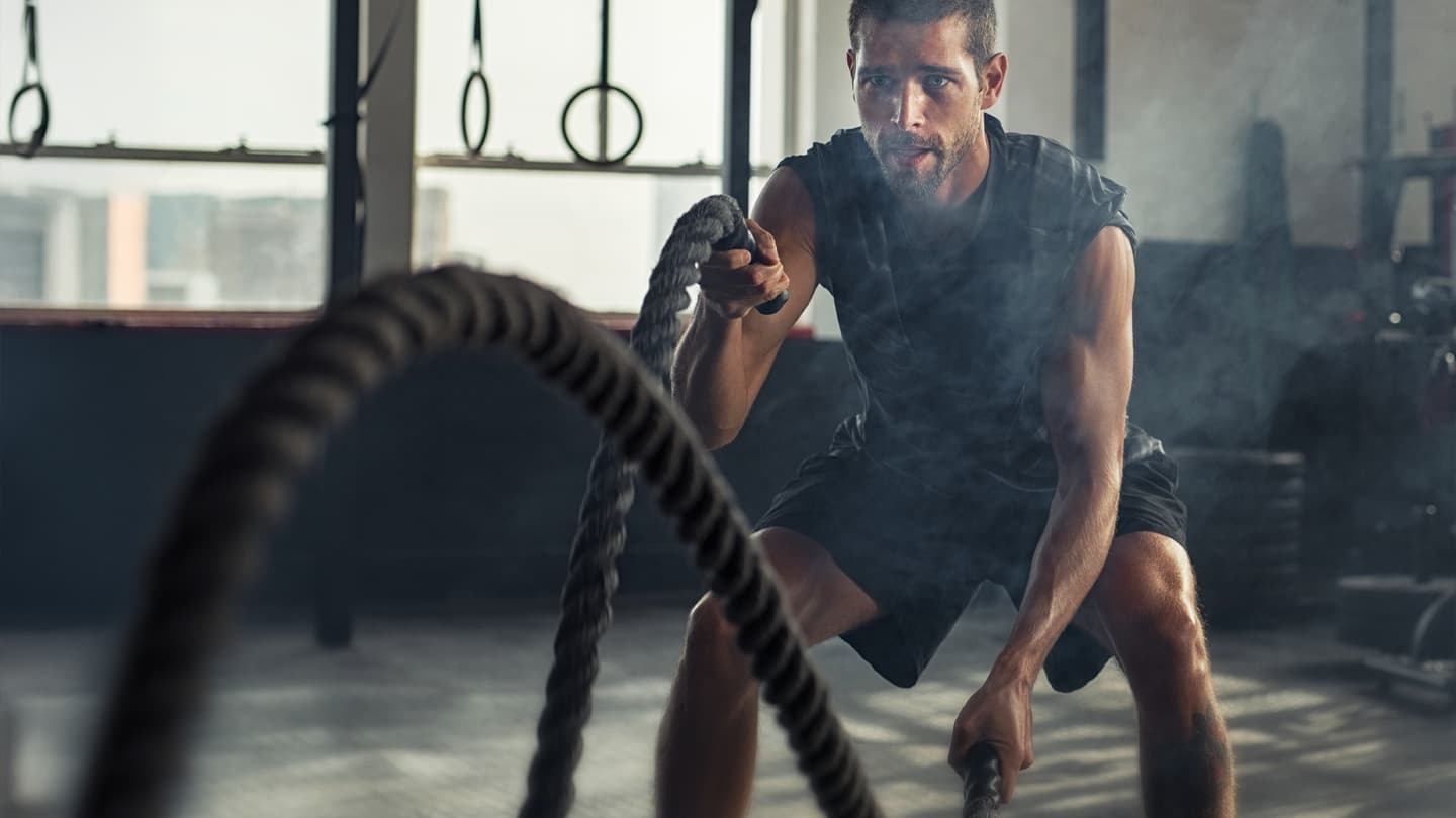 Intense Battle Rope Gym Workout Muscular man performing battle rope exercise in smoky gym