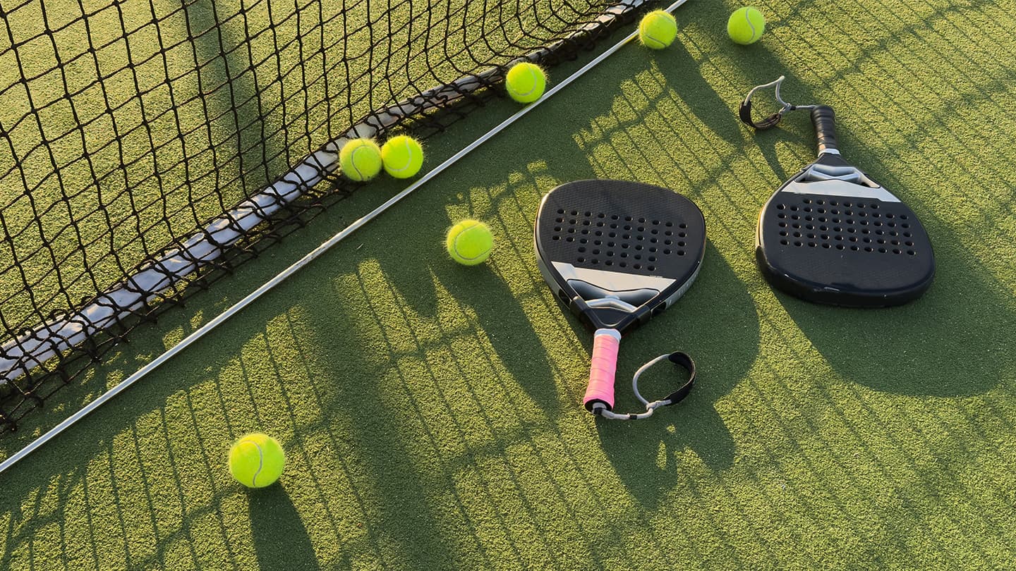 Paddle Tennis Equipment on Court Paddle tennis rackets with pink grip and yellow balls arranged on a green court next to the net.