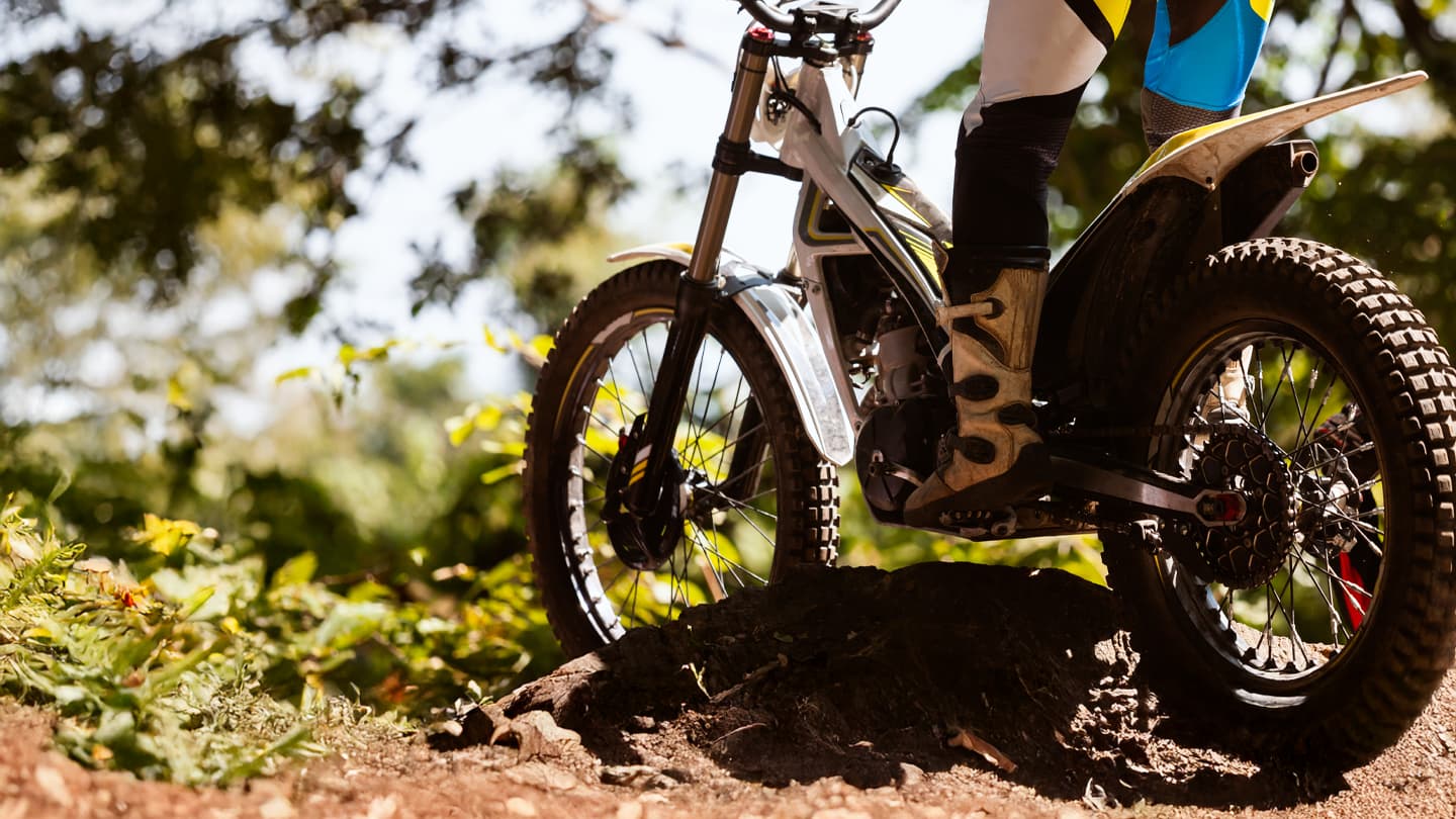 Trials Motorcycle on Off-Road Dirt Track Close-up of trials motorcycle navigating rocky dirt terrain in forest setting with rider in protective gear