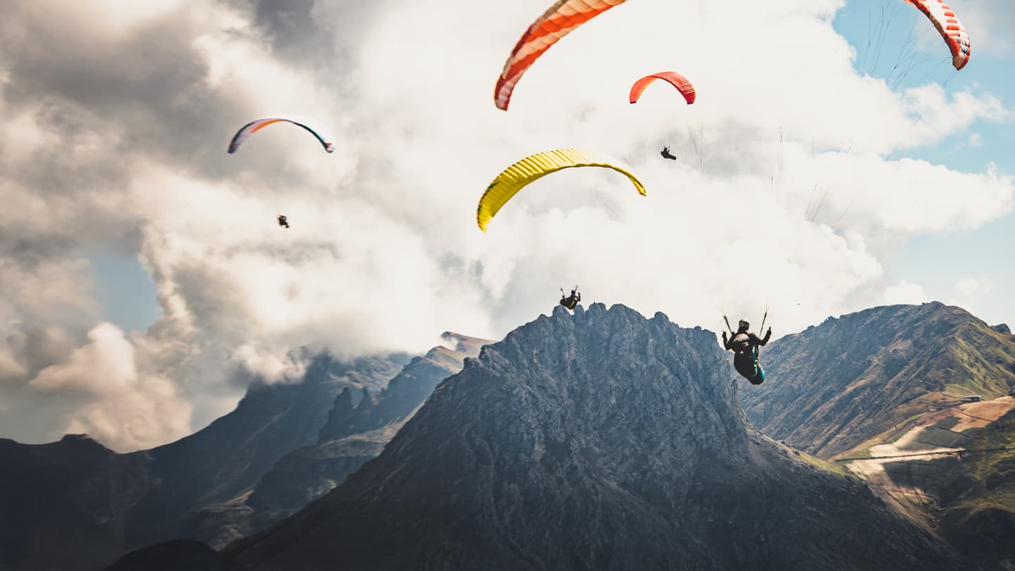 Paragliders Soaring Over Mountain Peaks Multiple colorful paragliders soaring above rugged mountain peaks against a dramatic cloudy sky
