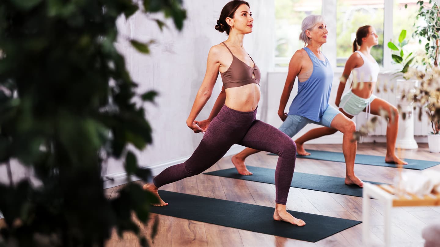 Women Practicing Yoga Lunge Pose Three women practicing warrior lunge pose during yoga class in a bright studio with plants