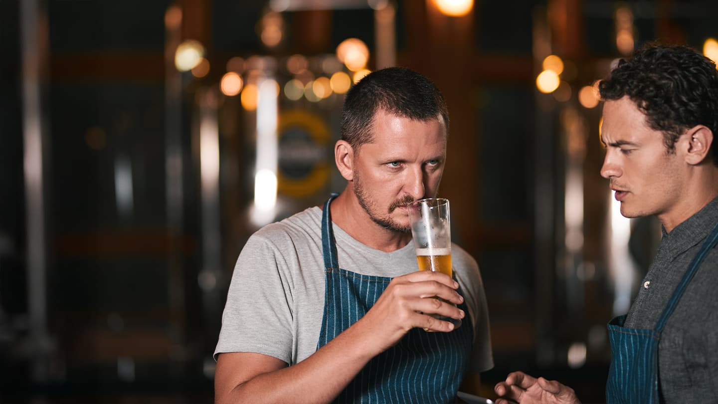 Craft Brewer Tasting Beer in Brewery Craft brewer tasting a pale ale beside fermentation tanks in a brewery