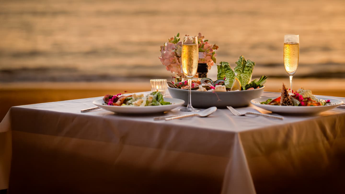 Romantic Beachside Dinner at Sunset Elegant romantic dinner table set for two on beach at sunset with champagne glasses and gourmet seafood dishes