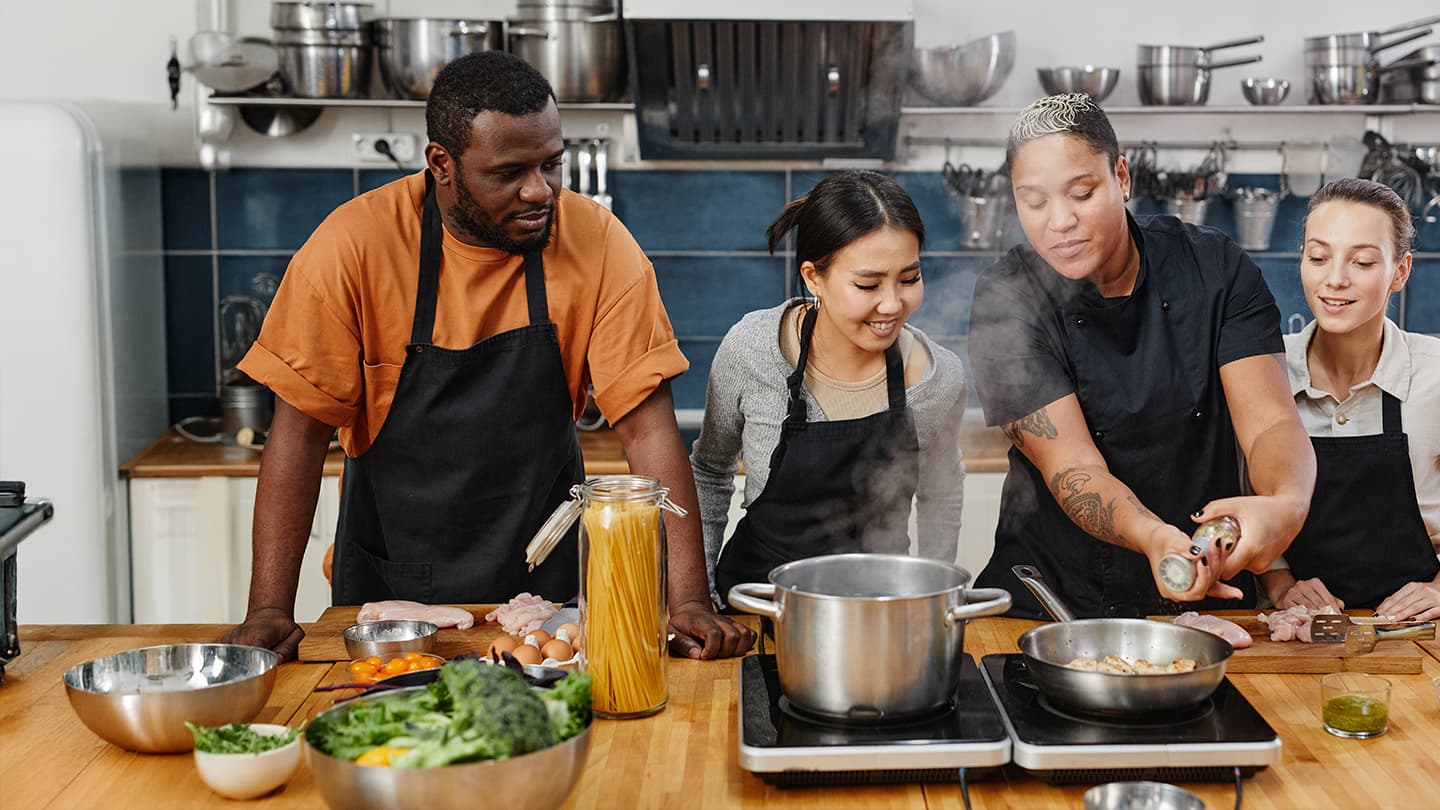 Hands-On Cooking Class with Chef Chef seasoning dish while three students watch during a cooking class