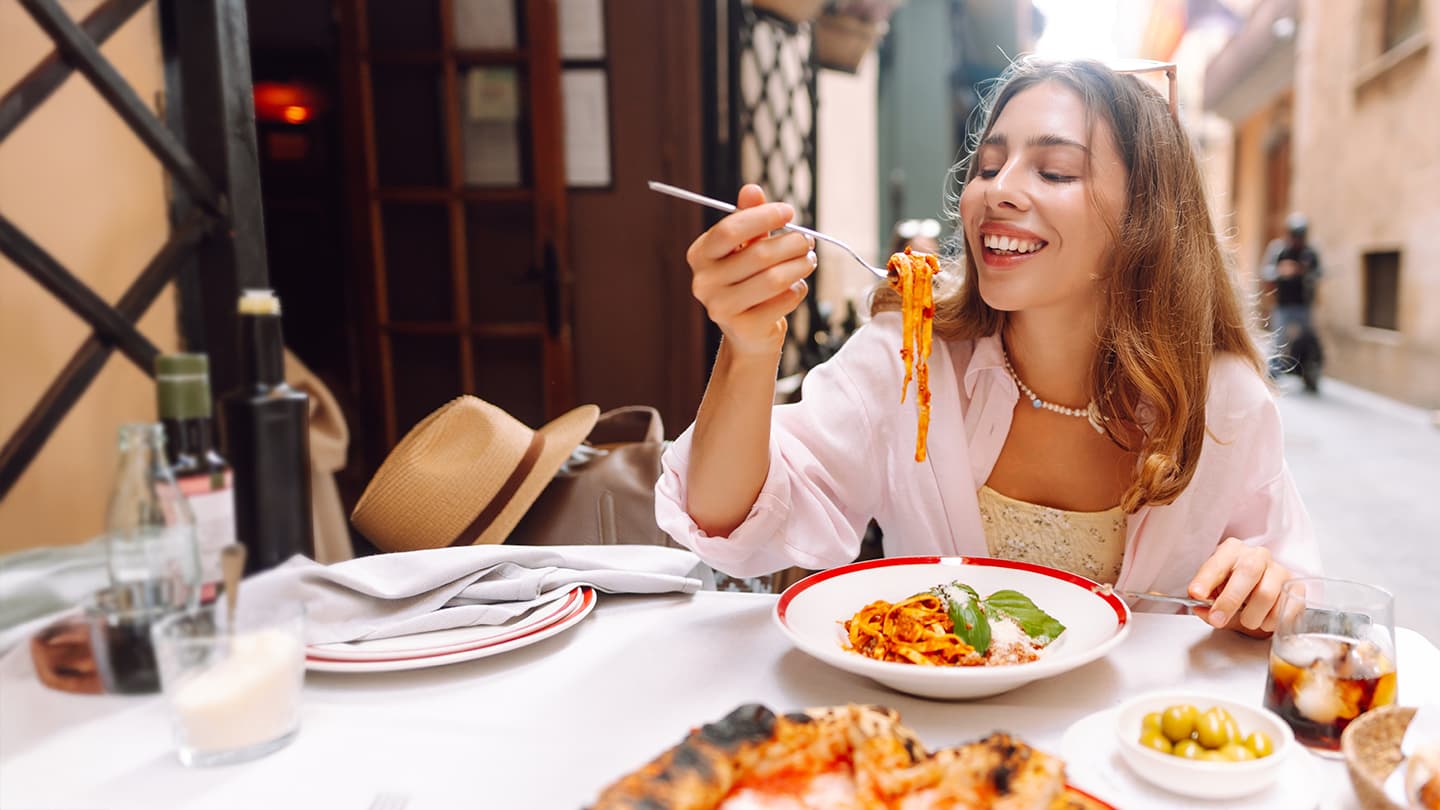 Outdoor Italian Dining Experience Smiling woman enjoying a pasta dish at an outdoor Italian restaurant