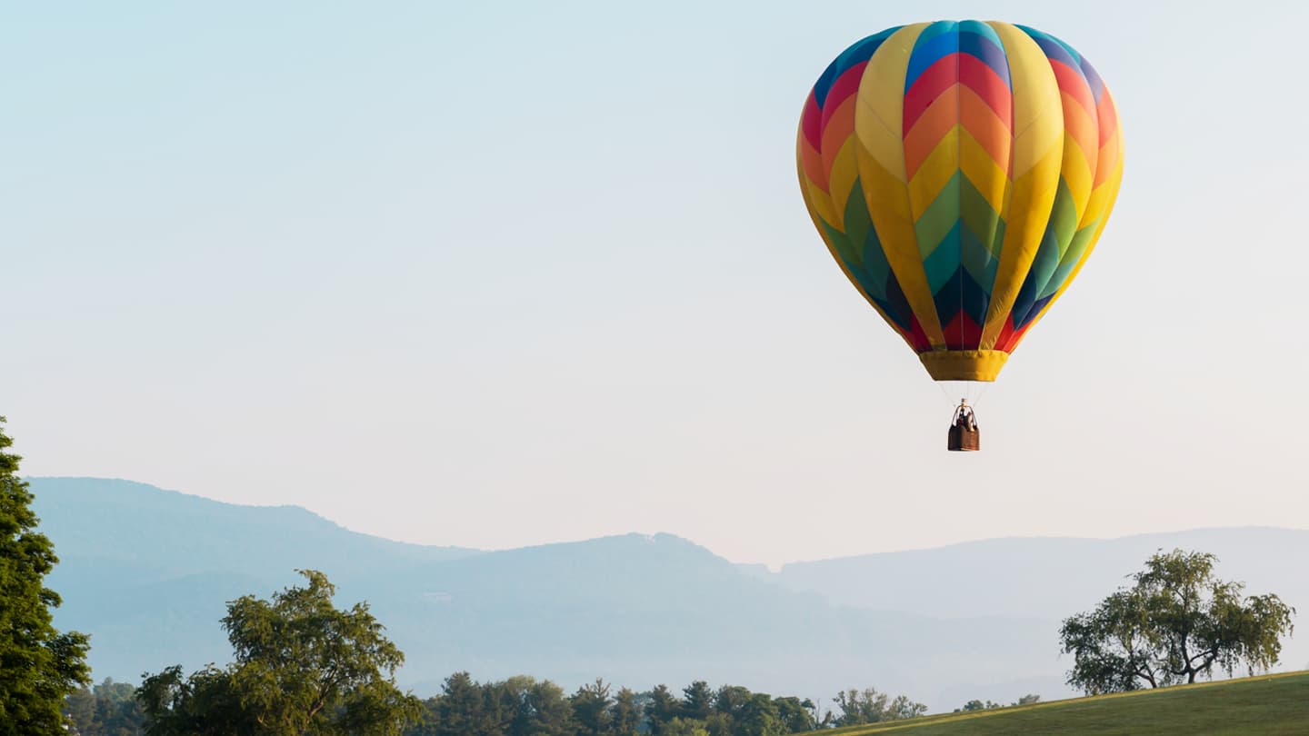 Colorful Hot Air Balloon Over Mountain Valley Vibrant multicolored hot air balloon floating above green trees with misty mountains in background