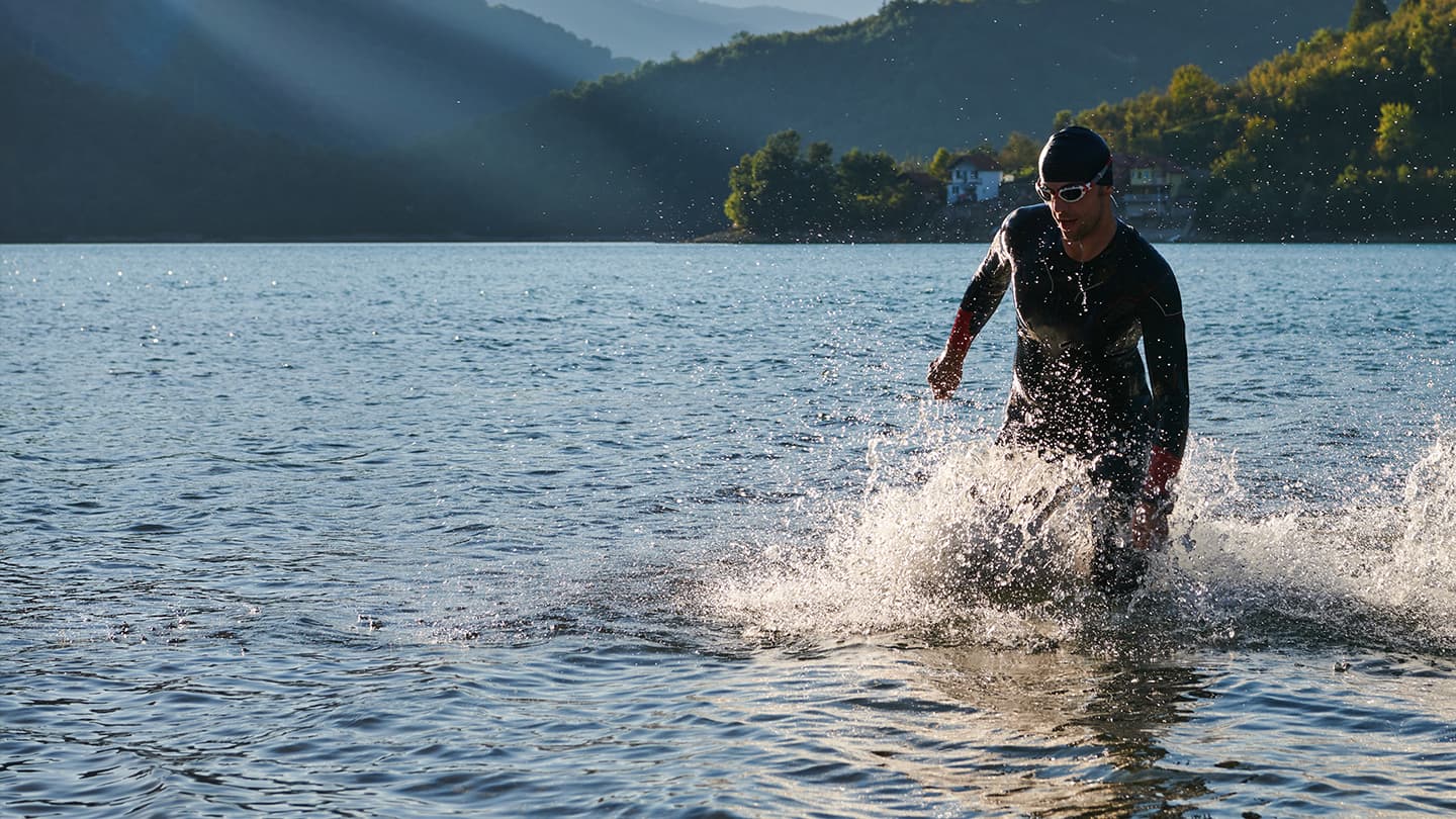 Open Water Triathlon Swim Exit Triathlete in wetsuit running out of a lake after open water swim