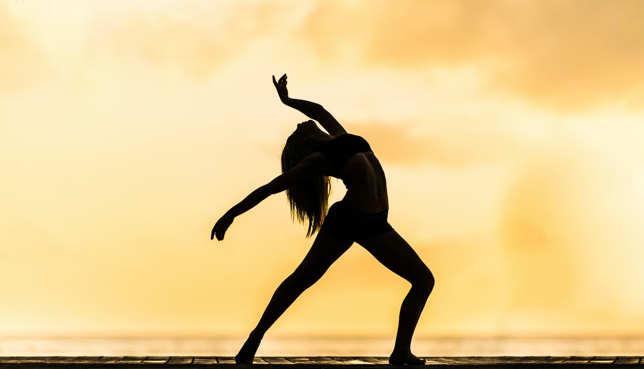 Dynamic Stretch Silhouette Against Golden Sky Silhouette of a person in a dynamic stretching pose against a golden sky backdrop.
