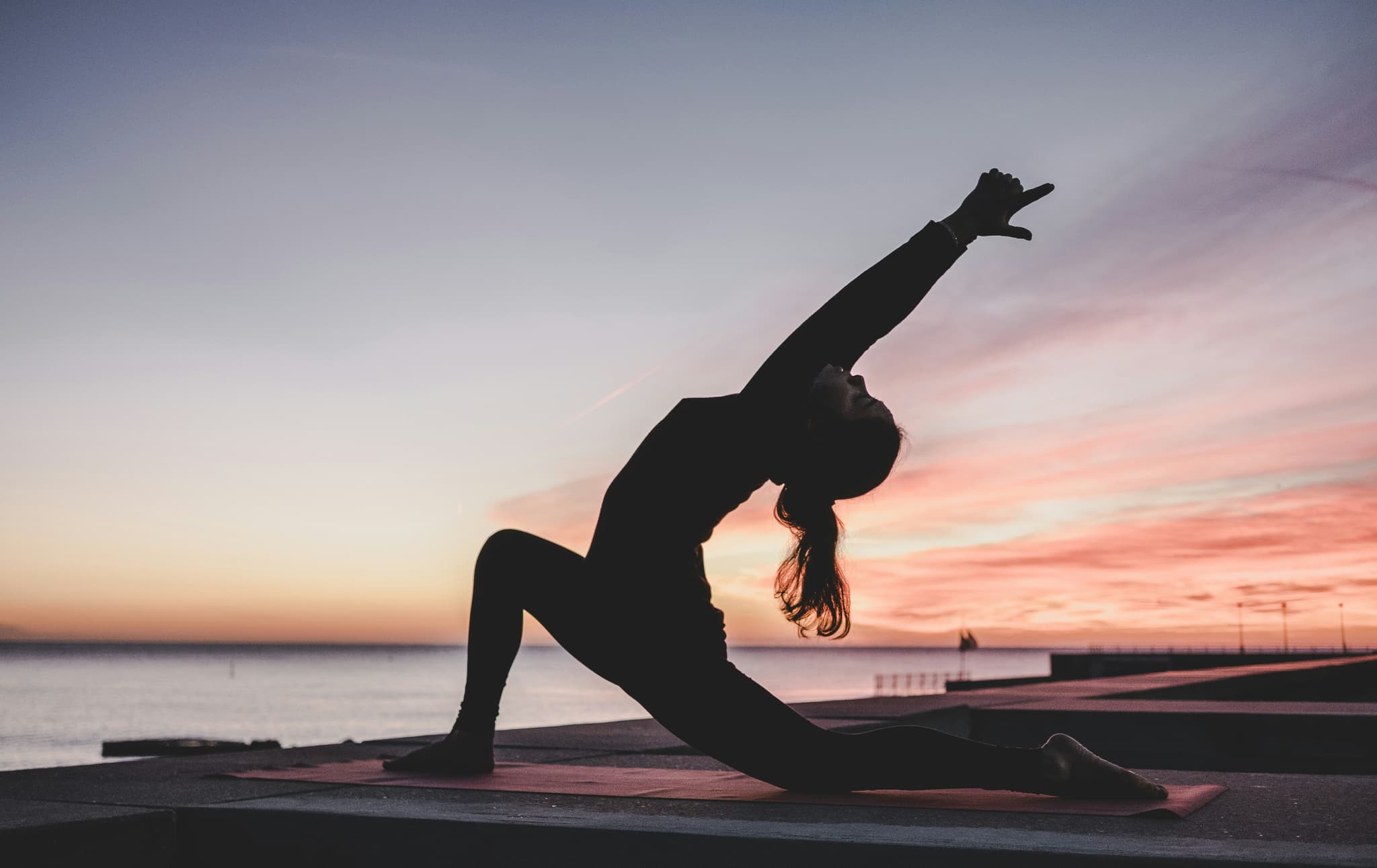 Yoga Practice at Beach Sunset Silhouette of a person in a yoga backbend pose on a beach at sunset, with calm water and a pier in the background.