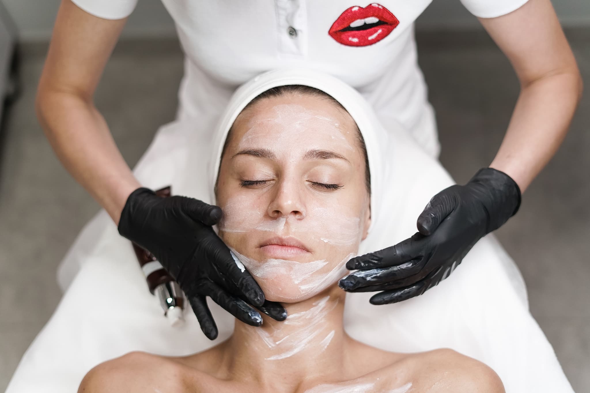 Facial Mask Treatment at Spa Person receiving a facial mask treatment from a skincare professional wearing black gloves.