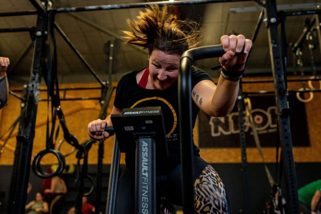Indoor Gym Workout on Assault Fitness Machine Person exercising on an Assault Fitness machine in an indoor gym with equipment and yellow wall backdrop.