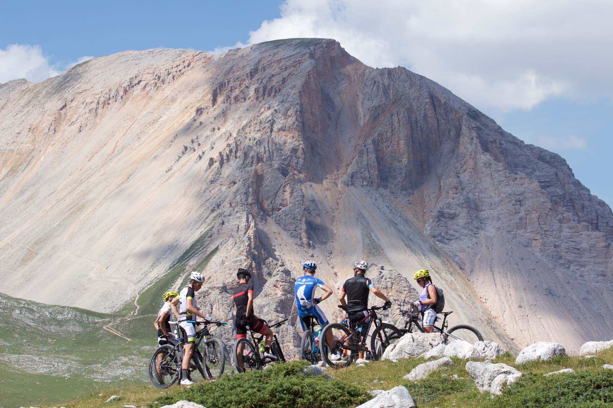 Mountainbiker auf Alpengipfel Gruppe von Radfahrern mit Fahrrädern auf einer Alpwiese, im Hintergrund ein dramatischer Felsgipfel.