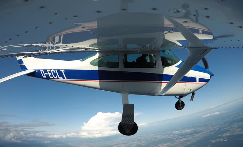 Small Aircraft in Flight Small aircraft in flight with blue and white livery, viewed from below against a clear sky with white clouds.