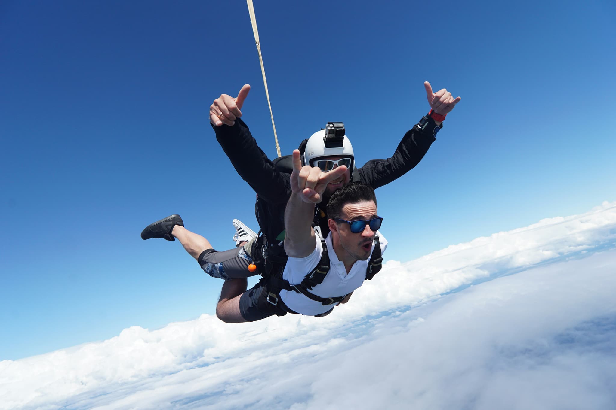 Tandem Skydive with Freefall Above the Clouds Two skydivers in freefall during a tandem jump, with clouds and blue sky below.