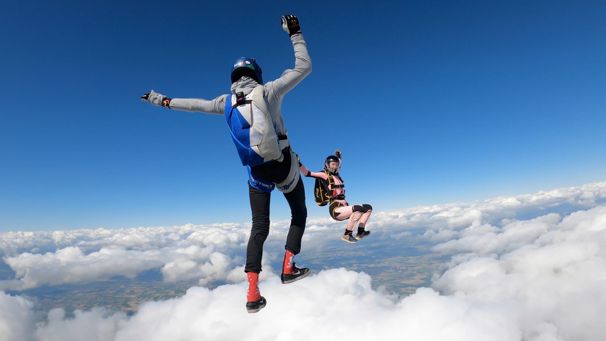 Skydivers in Freefall Above Clouds Two skydivers in freefall above a sea of white clouds with landscape visible below.