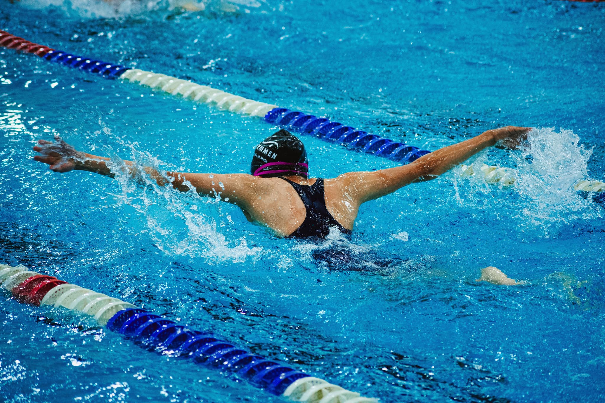 Swimmer Performing Butterfly Stroke Competitive swimmer performing butterfly stroke in a lap pool with lane dividers.