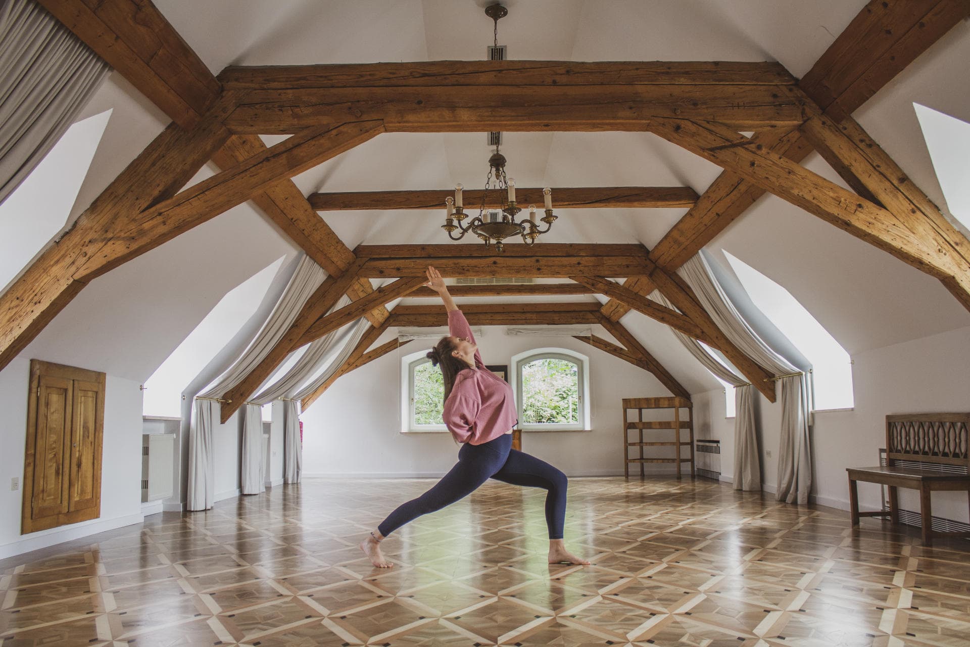Yoga Practice in Beam Studio Person in a yoga lunge pose inside a bright studio with exposed wooden beams and polished wooden floors.