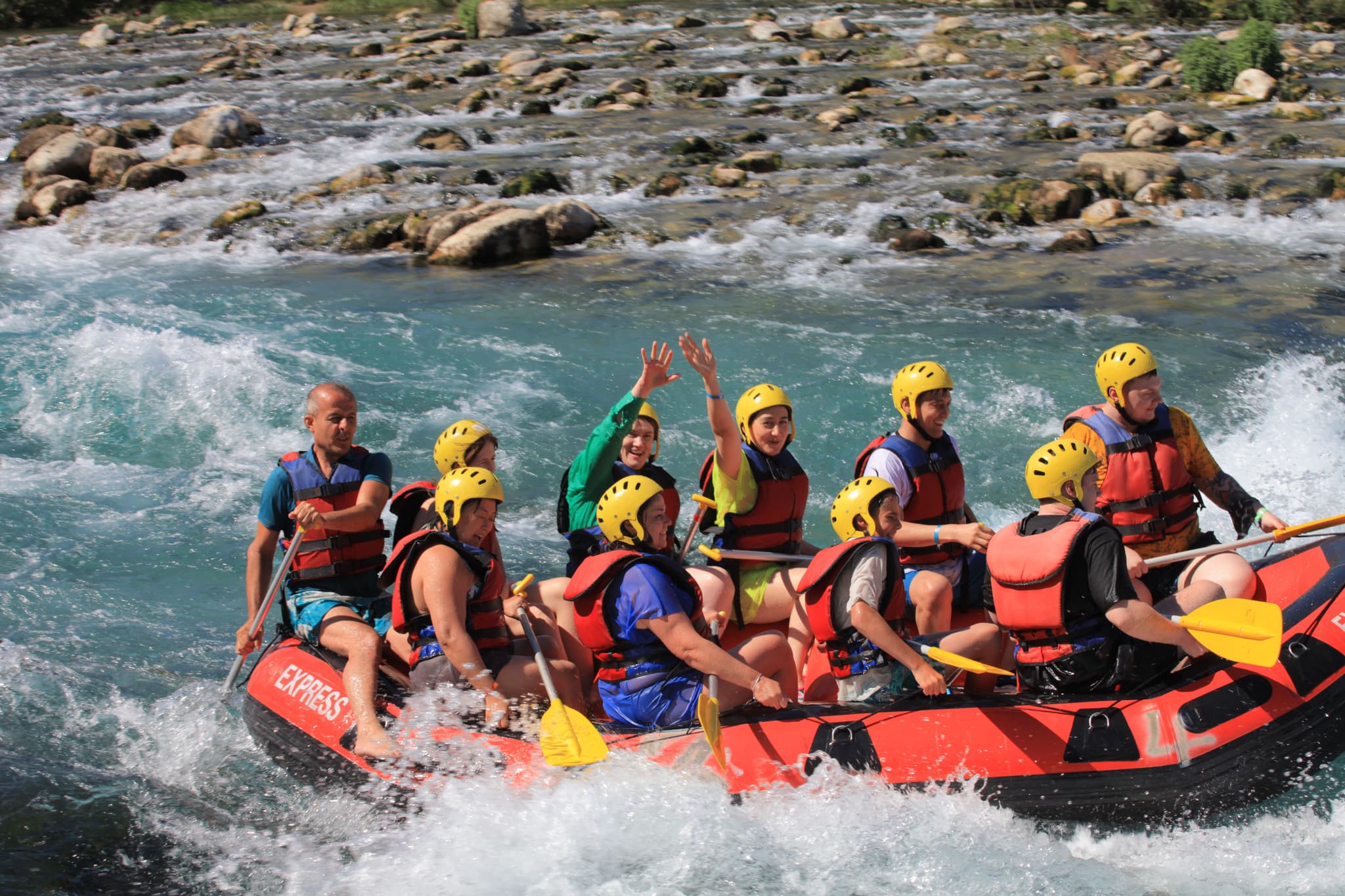 Whitewater Rafting in a Group on Rapids Group of people whitewater rafting on a turquoise river with rapids, wearing yellow helmets and red life jackets