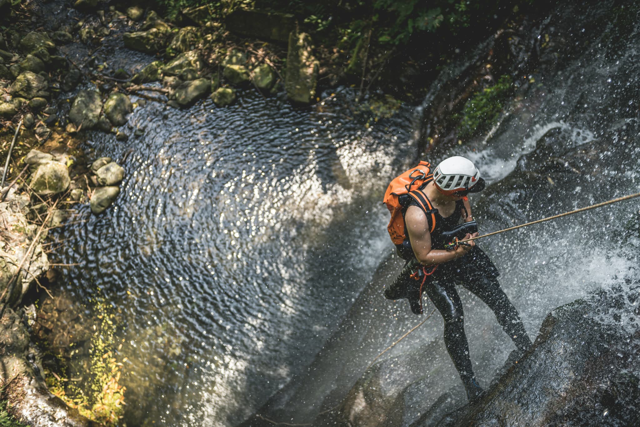Rappelling Down a Waterfall Person in orange safety gear rappelling down a waterfall in a rocky canyon.