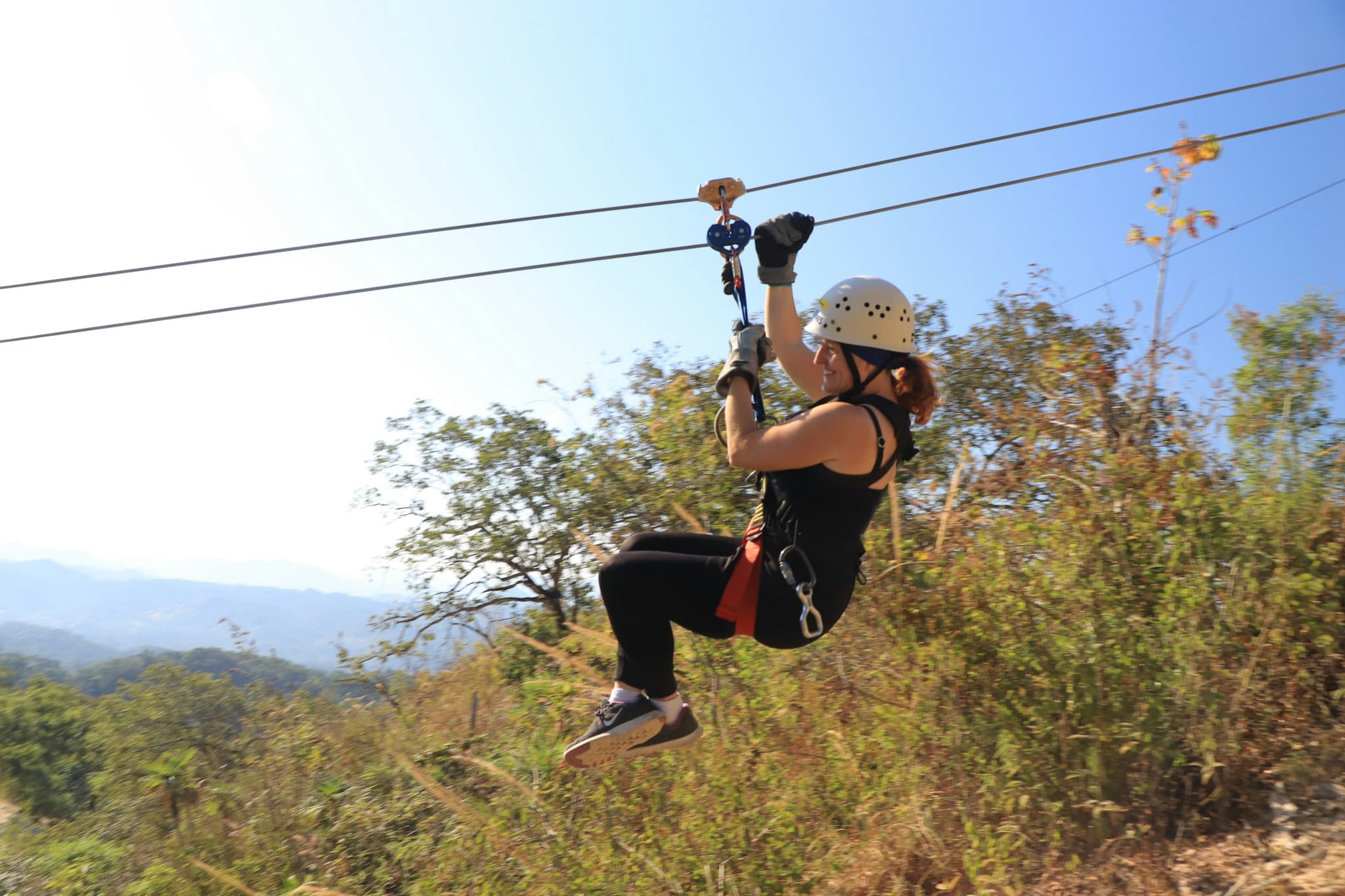 Ziplining Through Mountain Forest Person ziplining through a forested mountain landscape with a tan helmet and safety gear.