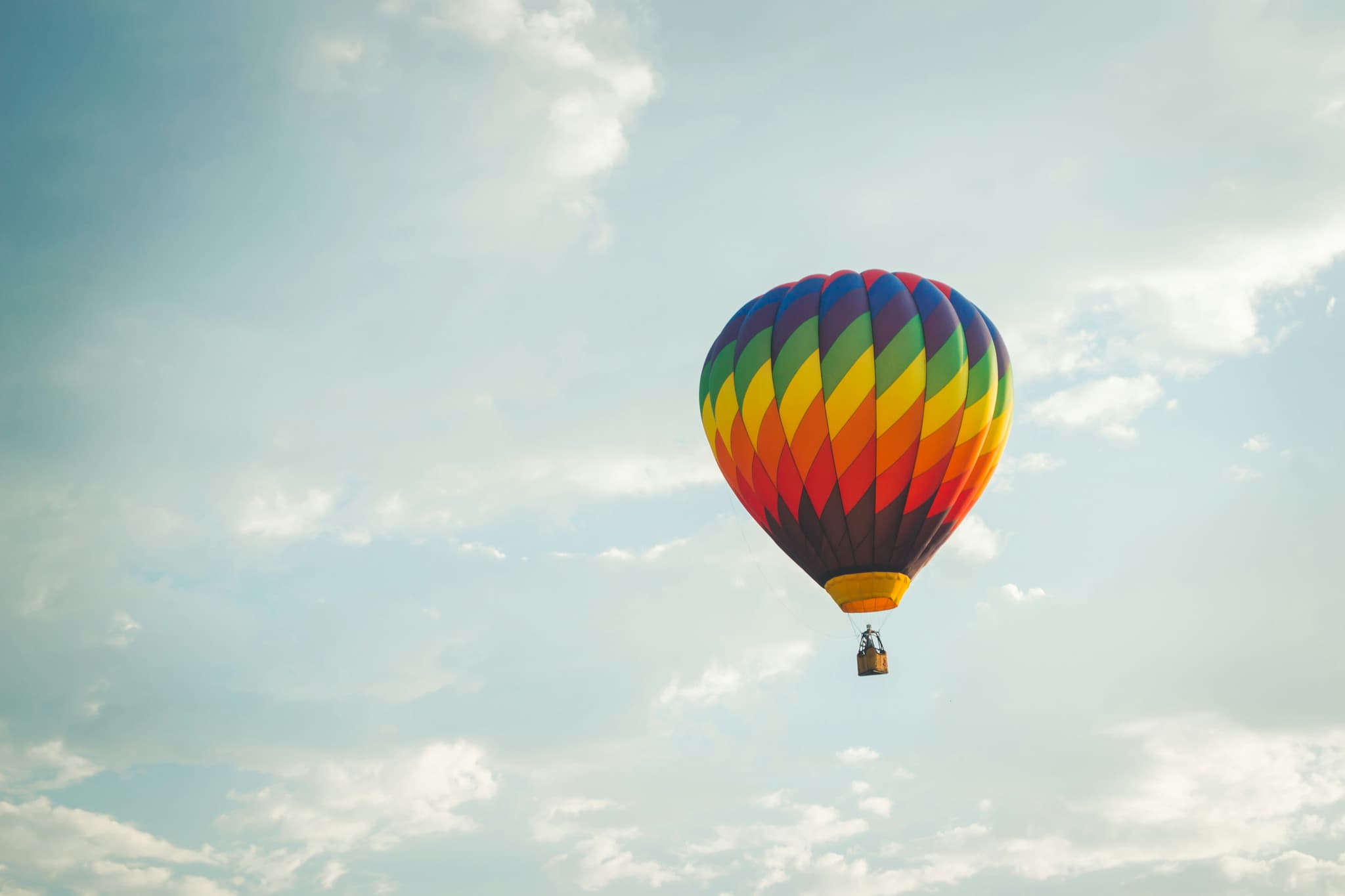 Hot Air Balloon in Blue Sky Colorful hot air balloon with red, blue, green, and yellow panels floating in a bright blue sky with white clouds.