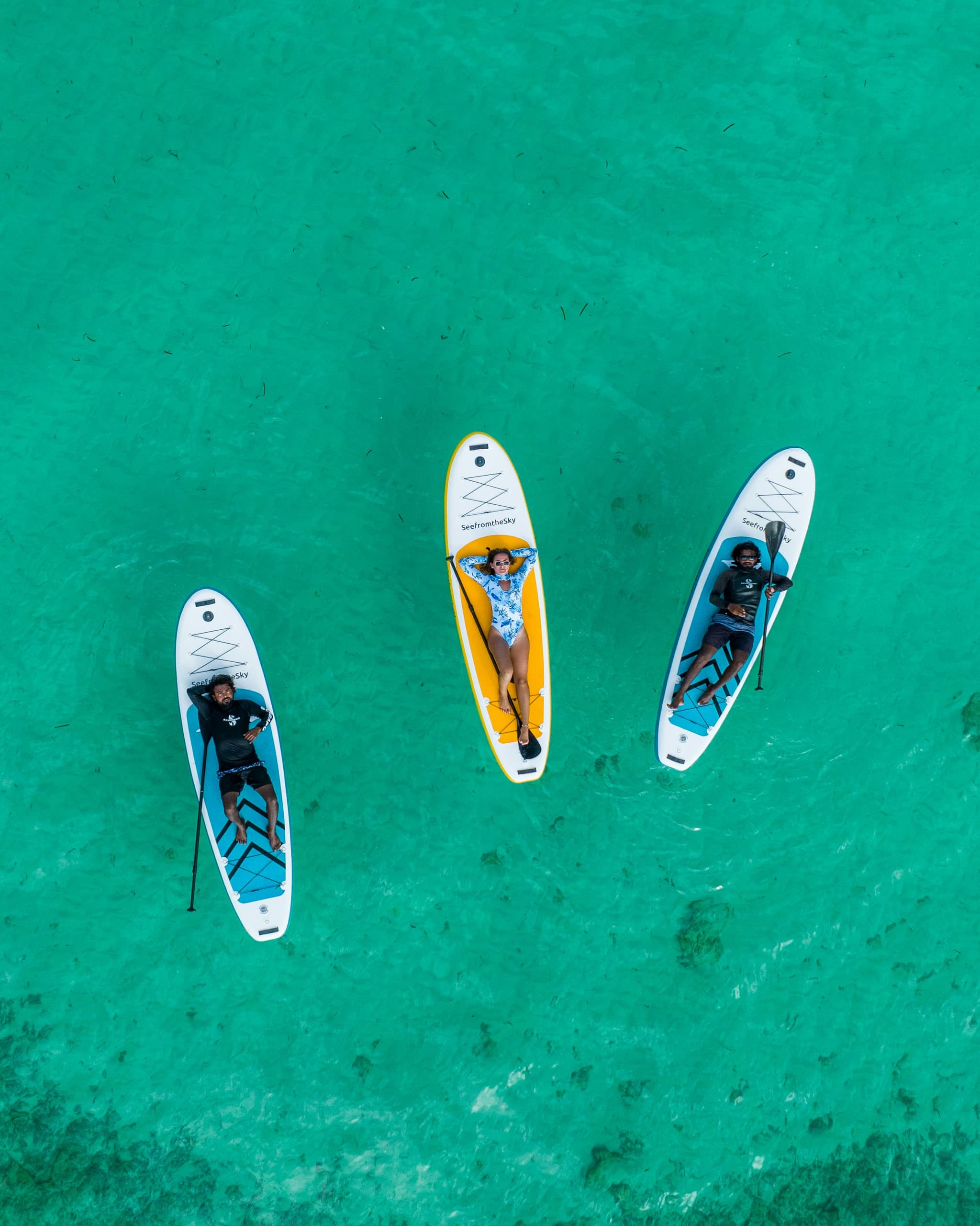 Paddleboarder in turquoise water Three paddleboarders on white and colorful boards in clear turquoise water, photographed from above.