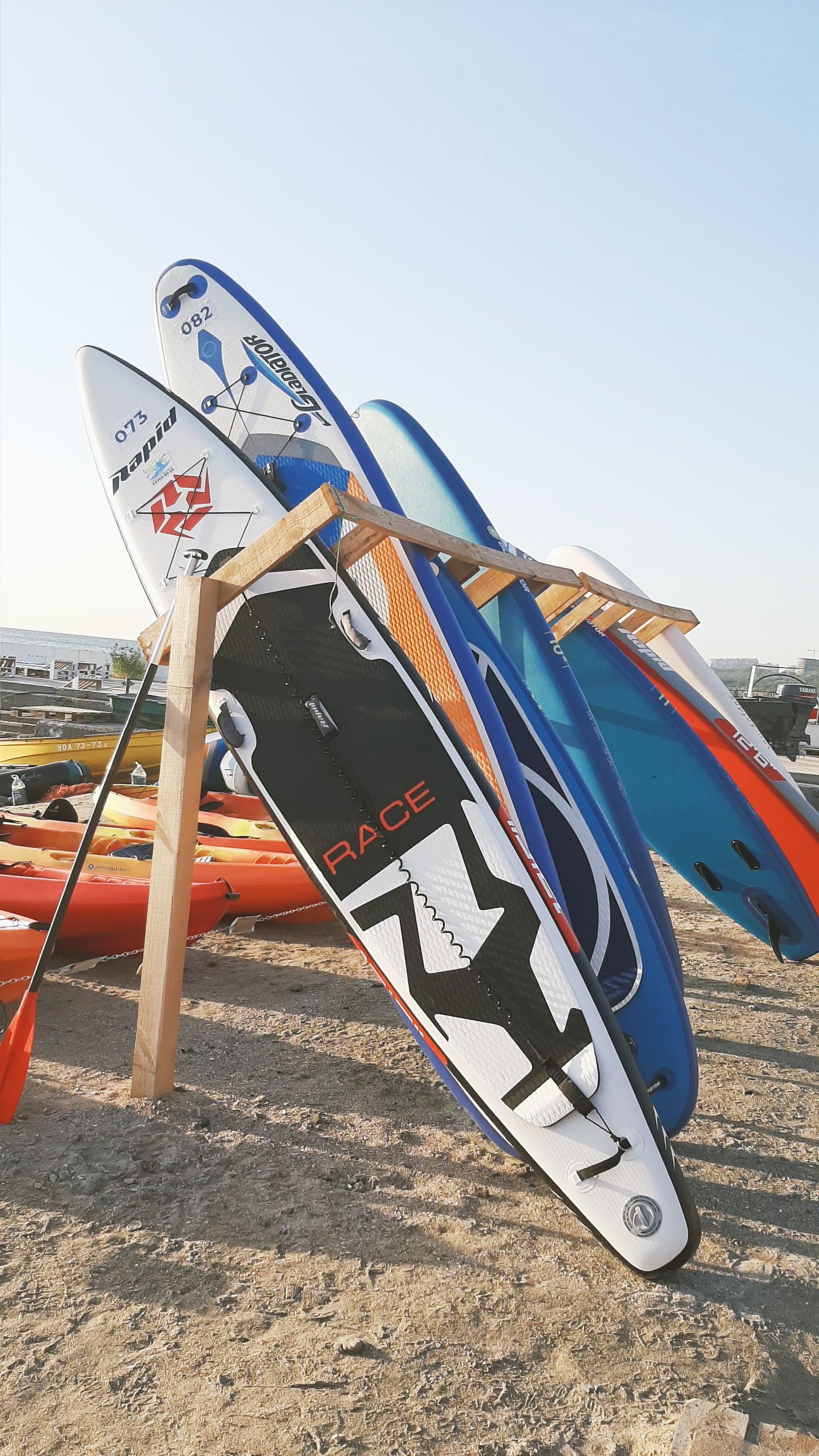 Kiteboarding Boards on Storage Rack Multiple kiteboarding boards displayed on a wooden rack at an outdoor water sports facility.