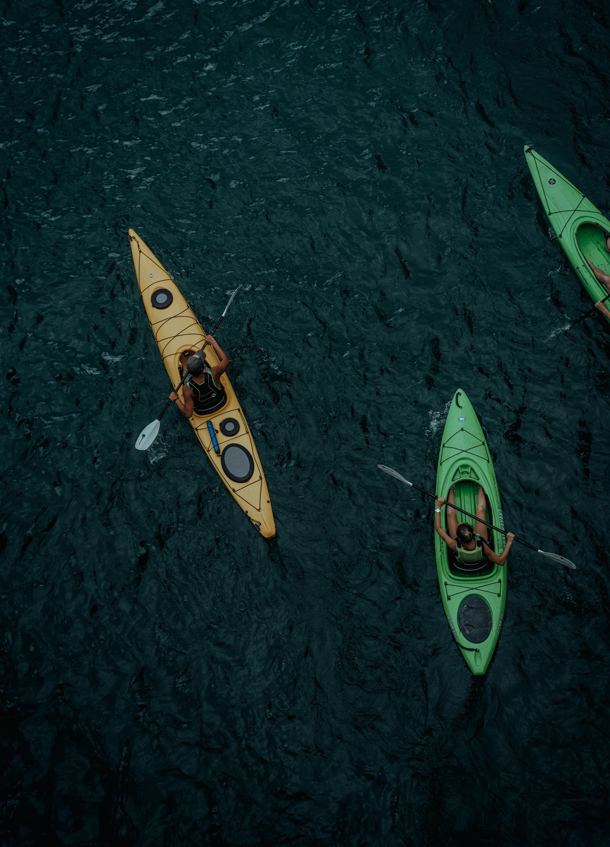 Kayakers on Dark Water Aerial View Aerial view of three kayakers in yellow and green kayaks on dark water.
