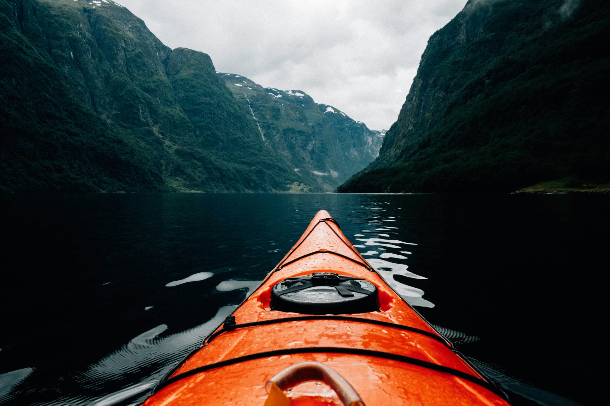 Kayak on Alpine Mountain Lake Orange kayak on a deep blue alpine lake surrounded by towering green mountain cliffs with waterfalls.