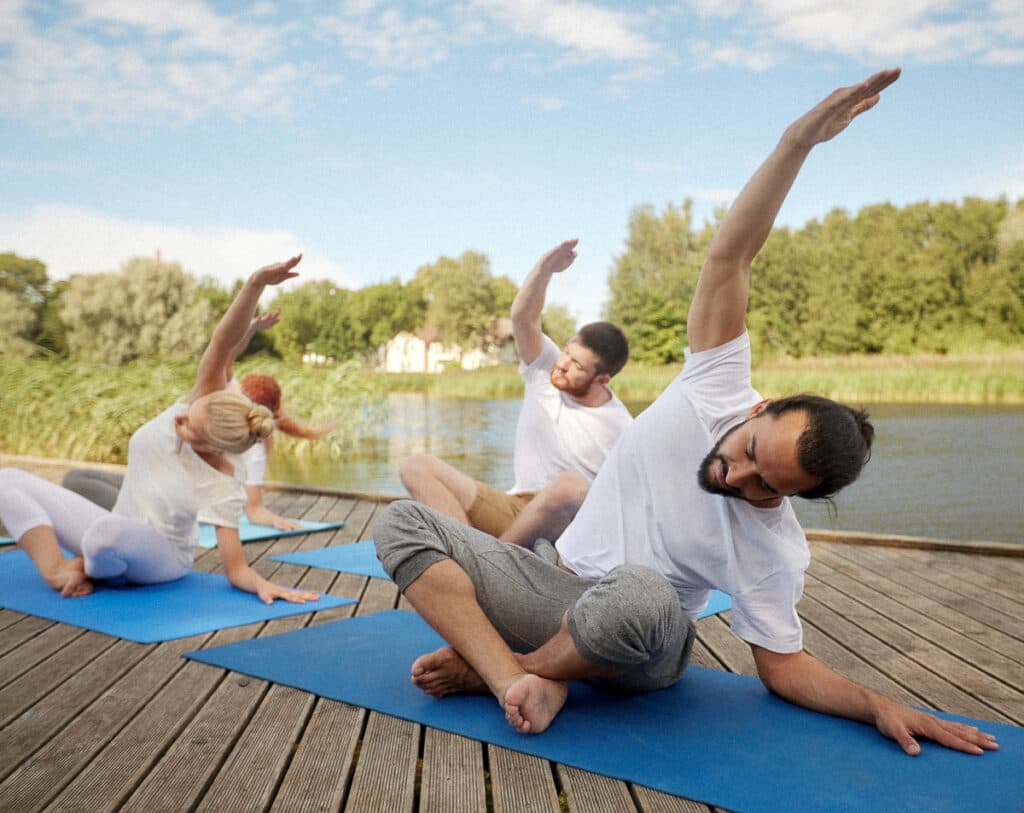 Outdoor Yoga Session by the Lake Group practicing seated side stretch yoga pose on mats along a lakeside deck.