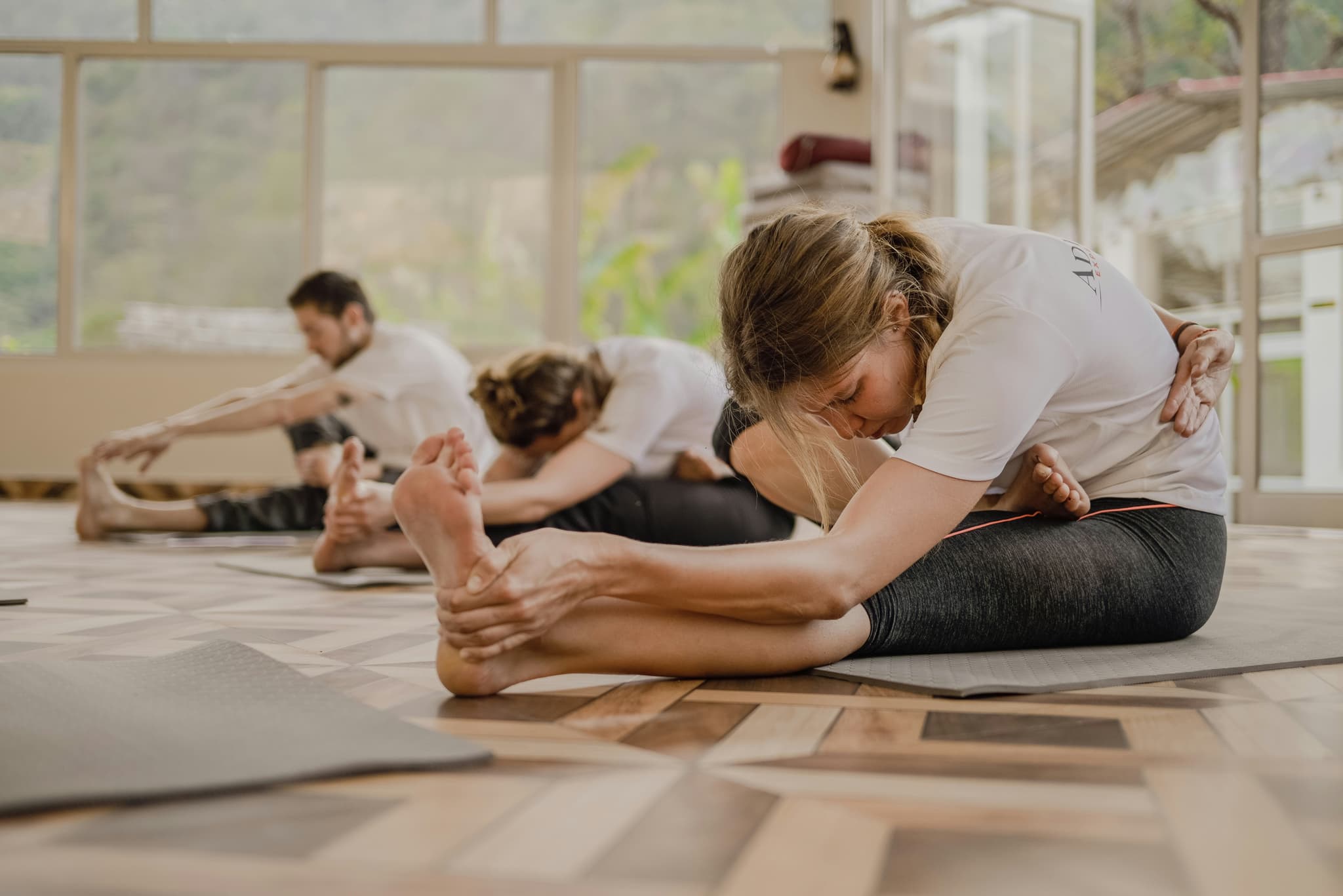 Group Forward Fold Stretch in Studio People in a studio doing seated forward fold stretches on yoga mats.